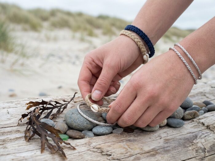 Trois bracelets marins posés sur du bois flotté avec des galets et des algues séchées sur une plage